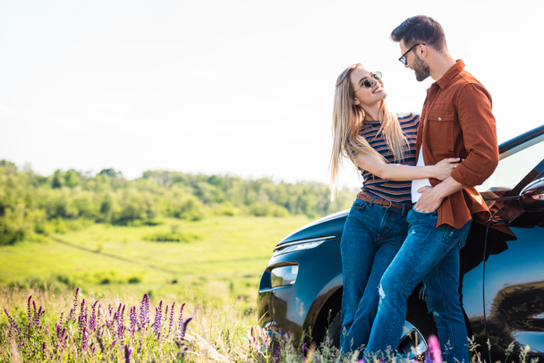 young stylish couple in sunglasses standing near car on rural meadow  - Fotó, kép
