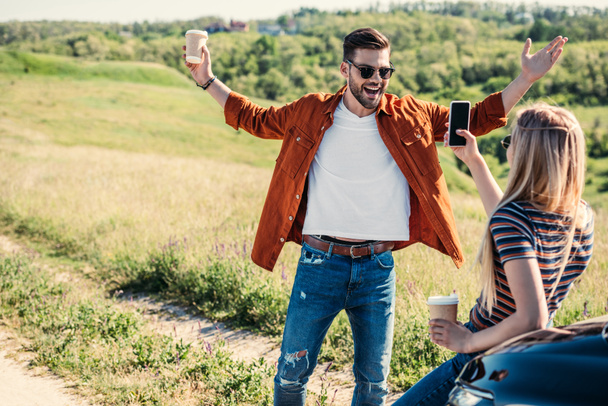 vista trasera de la mujer tomando foto de novio con brazos anchos sosteniendo taza de café cerca en prado rural
  - Foto, Imagen