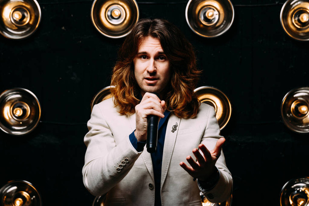 men singer with microphone on the stage, with long hair, against the background of bright lanterns, scene - Φωτογραφία, εικόνα