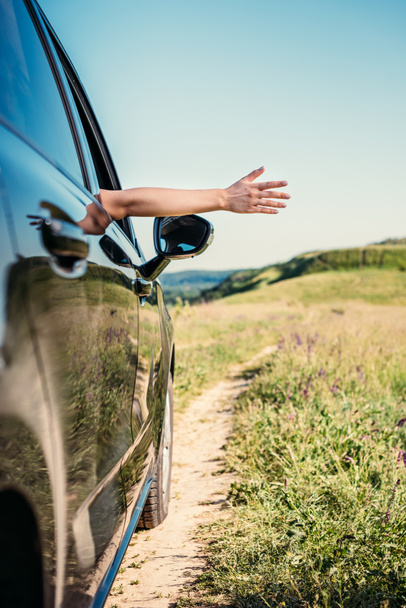 cropped shot of woman leaning out hand from car window in rural field  - 写真・画像