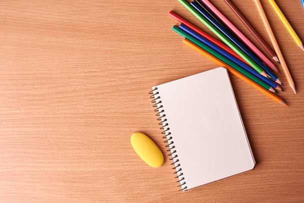 Откройте ноутбук на деревянном фоне с красочными карандашами. Плоский лежал
 - Фото, изображение