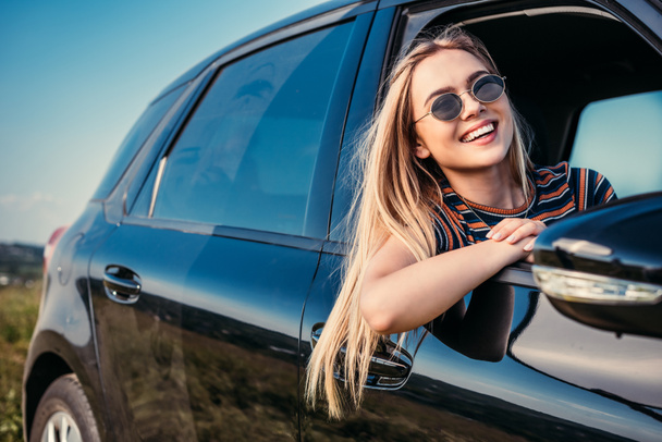 heureuse femme élégante dans les lunettes de soleil penché par la fenêtre de la voiture
  - Photo, image