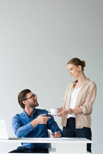 sorridente segretaria attraente passando tazza di caffè al capo isolato su bianco
 - Foto, immagini