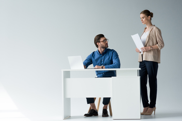 empresário sentado no local de trabalho, enquanto seu colega de pé com documentos atrás dele em branco
 - Foto, Imagem