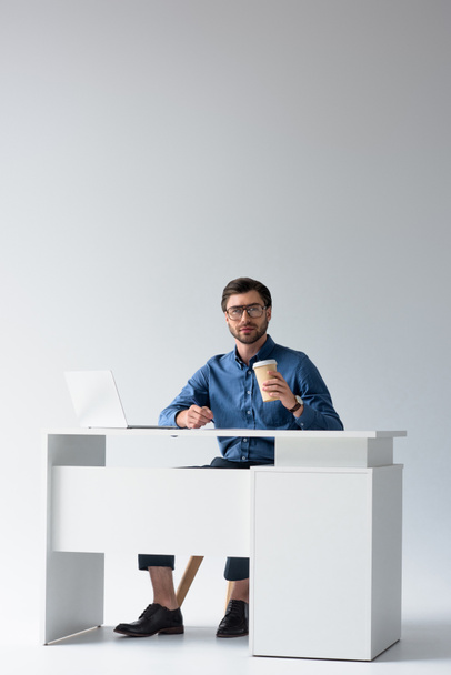 joven hombre de negocios guapo con portátil y café para ir en el lugar de trabajo en blanco
 - Foto, imagen