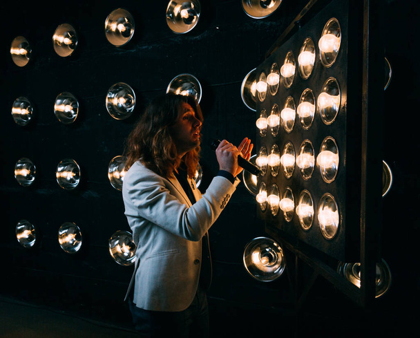 men singer with microphone on the stage, with long hair, against the background of bright lanterns, scene - Foto, imagen