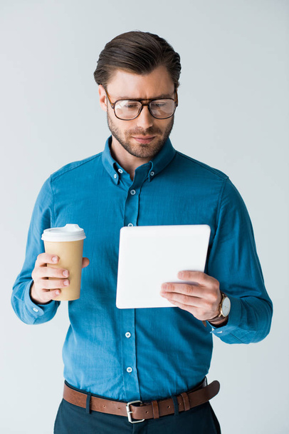 joven enfocado con taza de papel de café usando tableta aislada en blanco
 - Foto, Imagen