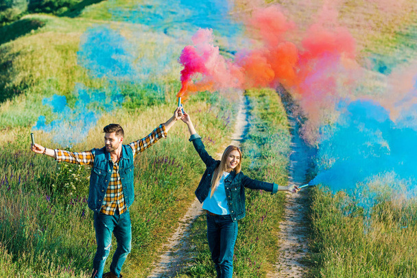 high angle view of young couple holding colorful smoke bombs on rural meadow  - Фото, зображення