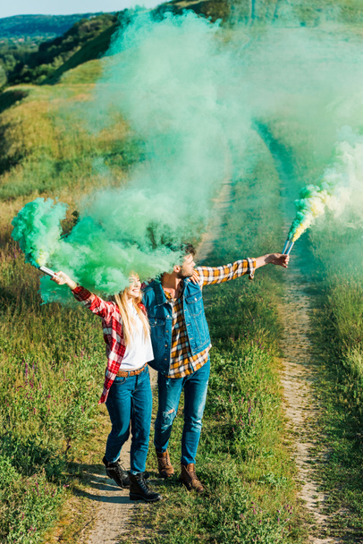 elevated view of young couple holding green smoke bombs in field - Photo, image