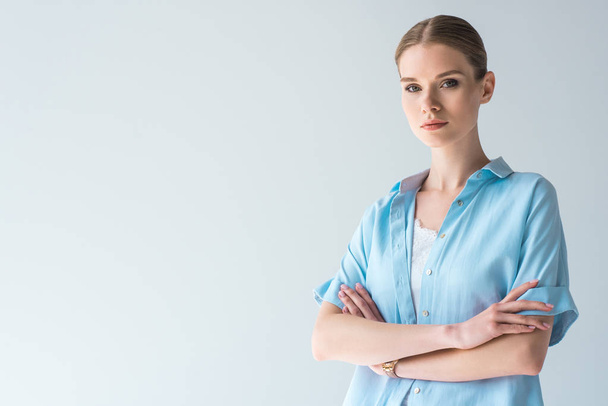 beautiful young woman in blue shirt with crossed arms isolated on grey - Photo, Image