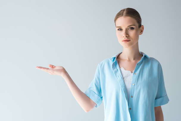beautiful young woman in blue shirt pointing at blank space isolated on grey - Photo, Image