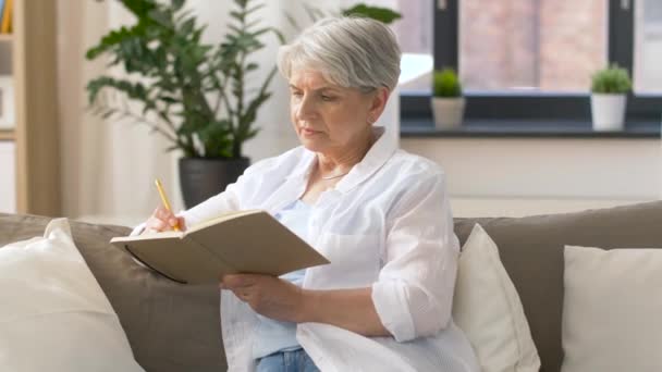 senior woman writing to notebook or diary at home - Video