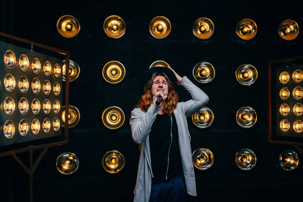 men singer with microphone on the stage, with long hair, against the background of bright lanterns, scene - Фото, зображення