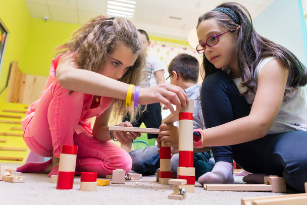 Due ragazze che giocano insieme con blocchi di giocattoli di legno sul pavimento all'asilo
 - Foto, immagini