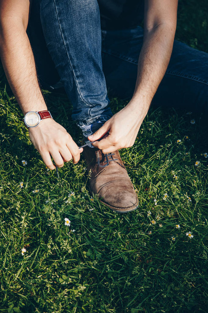 Детали снимка молодого человека, завязывающего свои стильные коричневые туфли
 - Фото, изображение