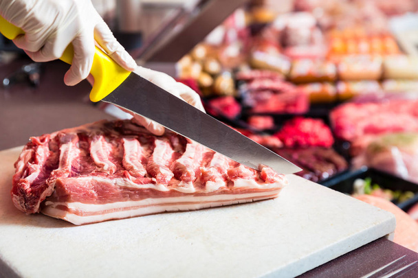 Butcher woman cutting piece of rib meat in her shop - Фото, изображение