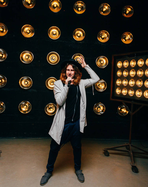 men singer with microphone on the stage, with long hair, against the background of bright lanterns, scene - Foto, imagen