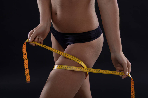 schlanke Frau, die ihr attraktives Bein auf schwarzem Hintergrund misst. Gewichtsverlust-Konzept - Foto, Bild