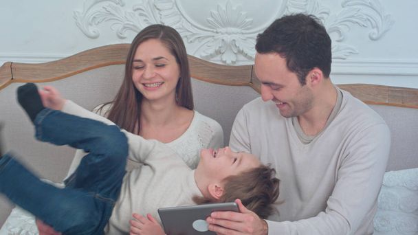 Happy family playing with their son sitting on the sofa while using digital tablet - Foto, Bild