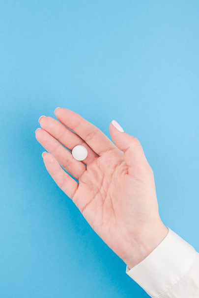 Woman hand holding a white pill on pastel blue paper background with copy space in minimal style, template for text. Concept of medical treatment, pharmacy, healthcare. - Photo, image