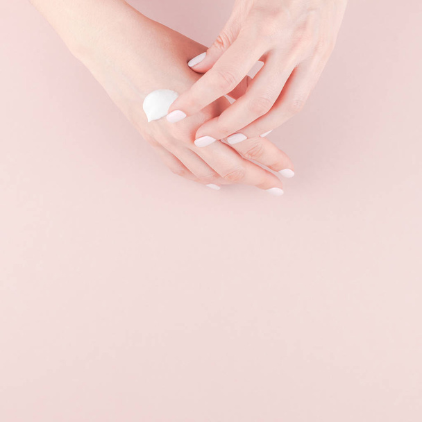 Creative image of woman moisturizing her hand with cosmetic cream lotion with copy space on millennial pink background in minimalism style. Square Concept for feminine blog social media beauty concept - Фото, изображение
