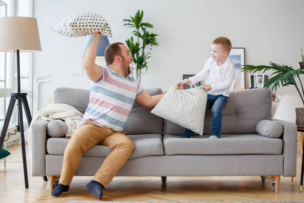 Photo of father fighting with son cushions on gray sofa - Fotó, kép