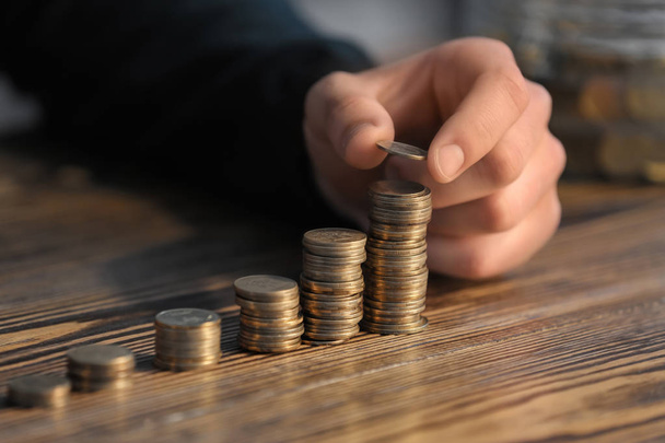 Mann stapelt Münzen auf Tisch. Sparkonzept - Foto, Bild