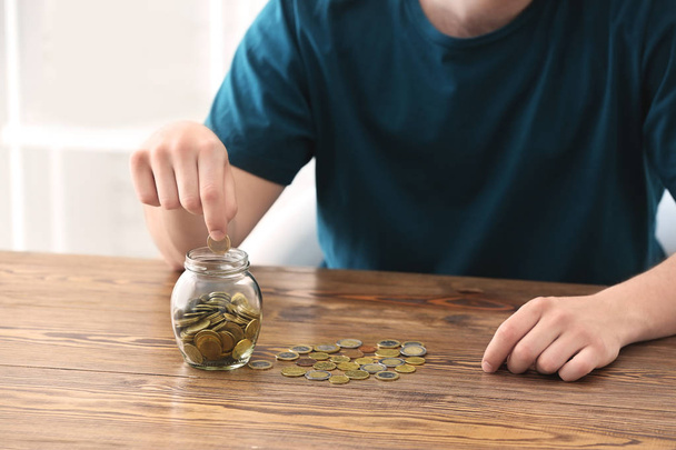 Man putting coins into glass jar on table. Savings concept - Photo, Image