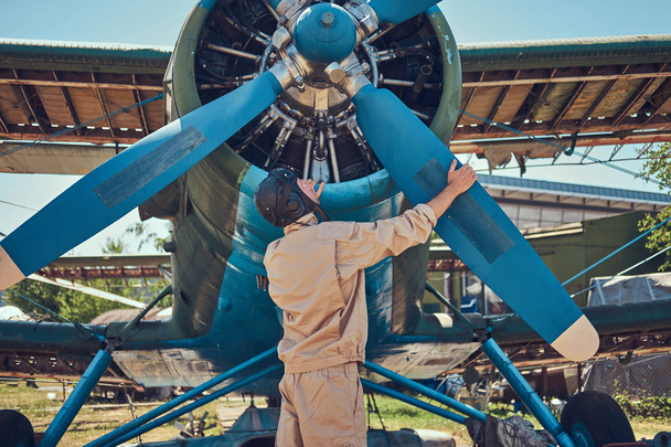 Pilot or mechanic in a full flight gear checks the propeller of his retro military aircraft before a flight. - Photo, Image