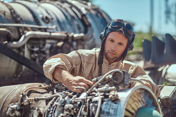 Portrait of a mechanic in uniform and flying helmet, repairing the dismantled airplane turbine in an open-air museum. - Photo, Image