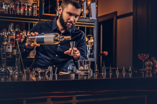 Stylish brutal bartender in a black shirt makes a cocktail at bar counter background. - Фото, зображення