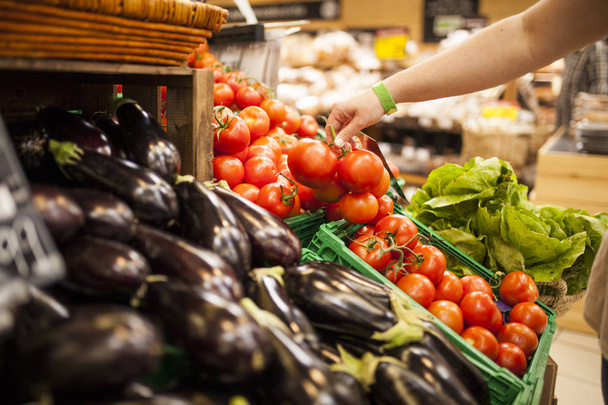 la mano de la mujer recogiendo tomates del mostrador de verduras en el supermercado
 - Foto, imagen