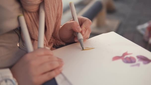 Vrouw is bloemenpatronen tekening in een schetsboek, zittend in een tuin, close-up - Video