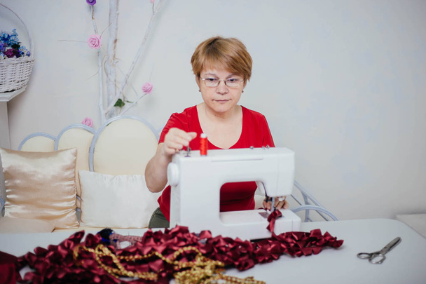 Una costurera con ropa roja cose en una máquina de coser. Atelier, el proceso de sastrería
. - Foto, Imagen