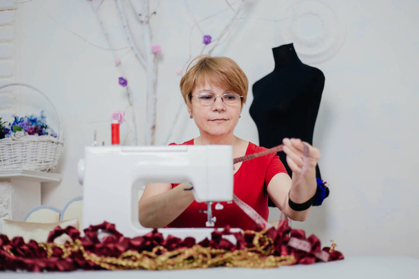 Una costurera con ropa roja cose en una máquina de coser. Atelier, el proceso de sastrería
. - Foto, imagen