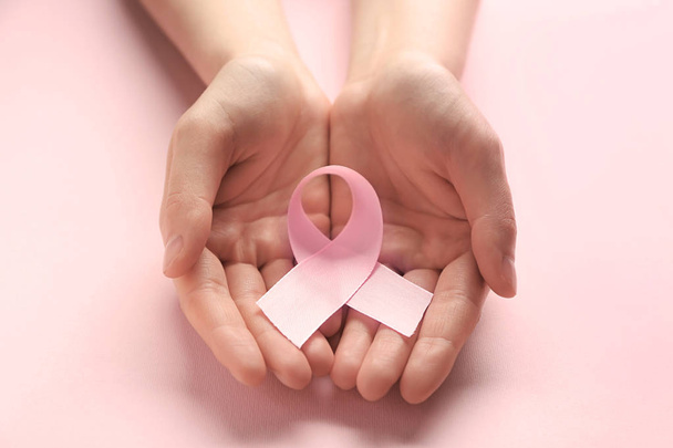 Female hands holding pink ribbon on color background. Breast cancer awareness concept - Photo, Image