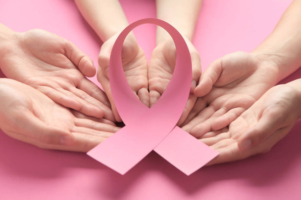 weibliche Hände mit rosa Schleife auf farbigem Hintergrund. Brustkrebs-Aufklärungskonzept - Foto, Bild