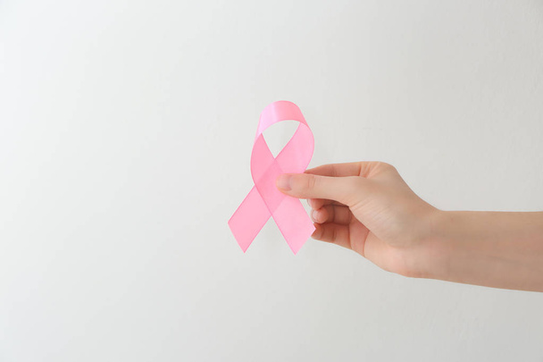 Female hand holding pink ribbon on light background. Breast cancer awareness concept - Photo, Image