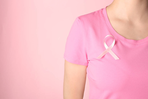 Woman with pink ribbon on t-shirt against color background. Breast cancer awareness concept - Fotó, kép