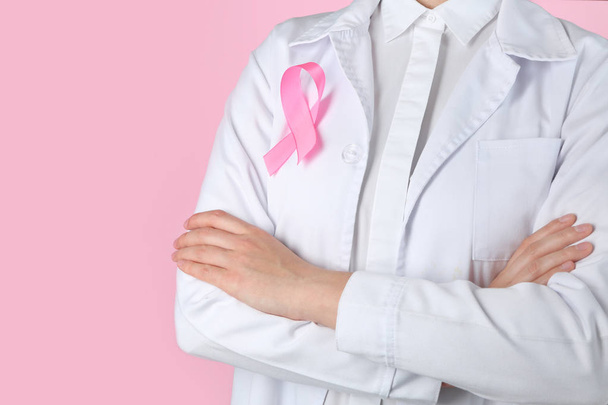 Médico con cinta rosa en la bata contra el fondo de color. Concepto de conciencia sobre el cáncer de mama
 - Foto, Imagen