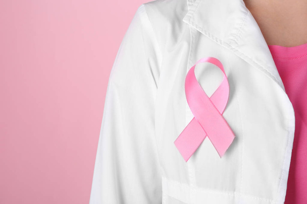 Doutor com fita rosa em roupão contra fundo de cor, close-up. Conceito de consciência do câncer de mama
 - Foto, Imagem