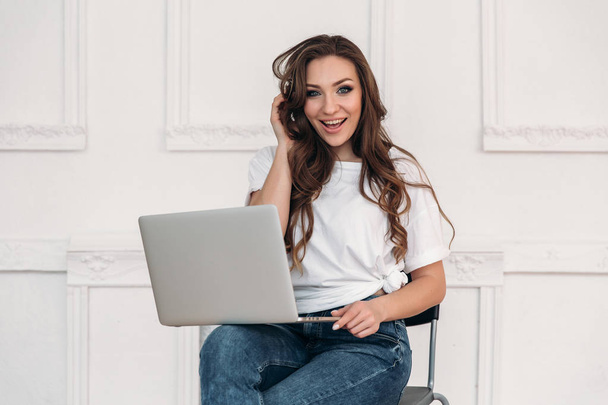 A cheerful smiling slender woman working on a laptop, put it on her lap. An attractive freelancer earns money in any conditions, even without an office. - Foto, Imagen