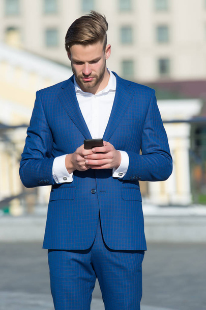 Message concept. Man in suit businessman takes advantages of modern mobile technologies. Man reads message mobile phone. Businessman serious face received important message, urban background. - Фото, изображение