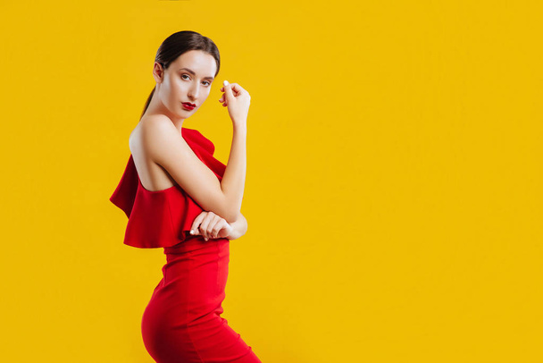 Beautiful woman posing in red dresover yellow background. - Фото, изображение