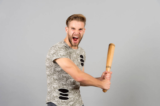 Bully man shouting aggressive face, grey background. Man with wooden bat ready to attack. Aggressive behaviour concept. Man bearded looks aggressive and threatening. Dangerous behaviour of hooligan - Foto, Imagem