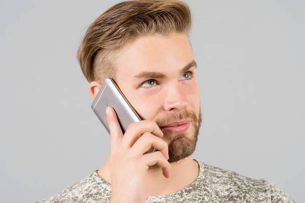 Man thoughtful dreamy use smartphone communication, grey background. Communication concept. Guy attractive well groomed with beard and hairstyle talk on smartphone. Man having mobile conversation - Photo, image