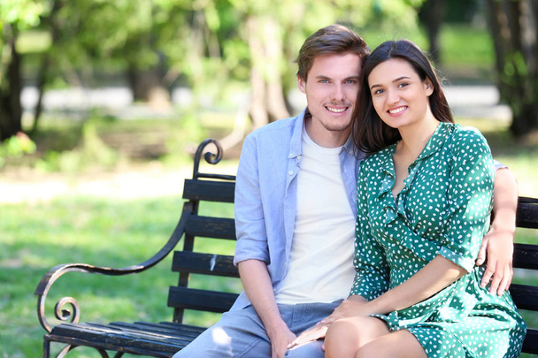 Jeune couple reposant sur un banc dans un parc verdoyant
 - Photo, image