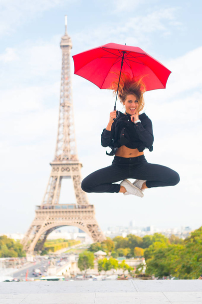 Dreams come true concept. Lady tourist sporty and active in Paris city center jumps up. Girl tourist enjoy walk and sightseeing. Lady with umbrella excited about visiting Eiffel Tower, sky background - 写真・画像
