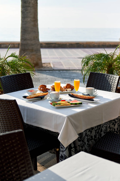 Outdoors restaurant. Table setting with classic breakfast. Orange juice, fruits and pastries - Zdjęcie, obraz
