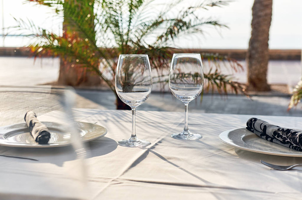 Table setting with a wine glasses, cutlery and plates. Outdoors restaurant. Tropical landscape - Fotoğraf, Görsel